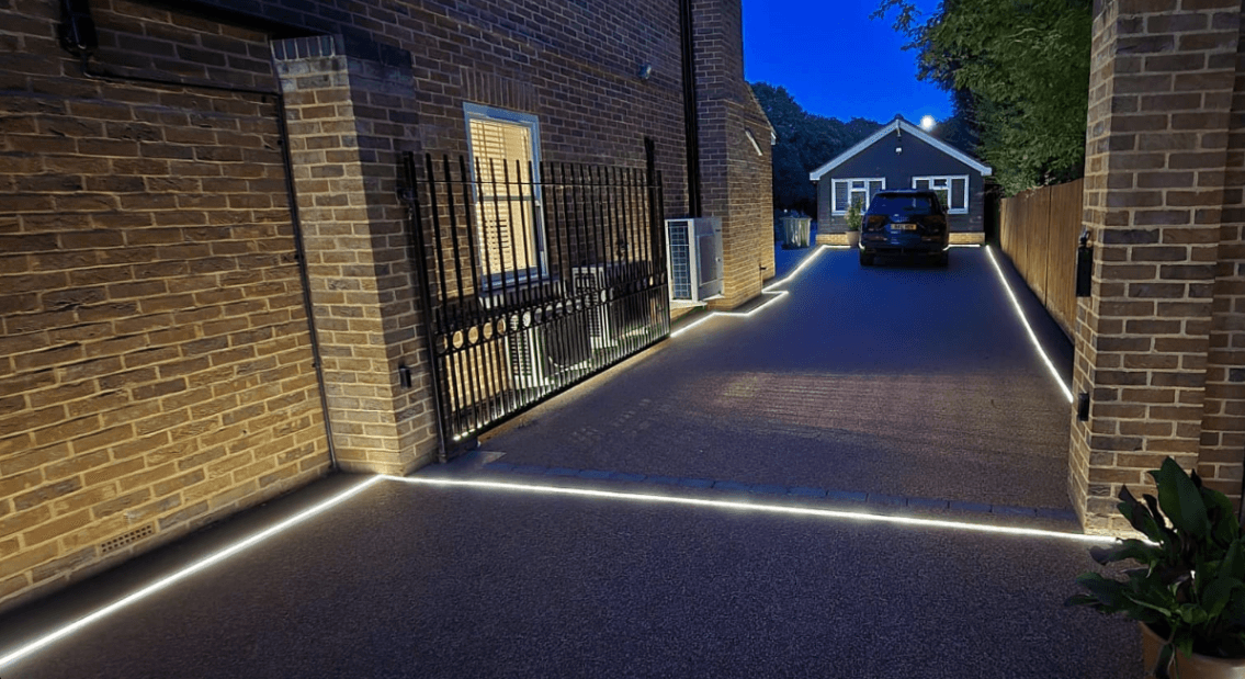 Modern driveway at night featuring bright white LED strip lighting embedded in the ground.